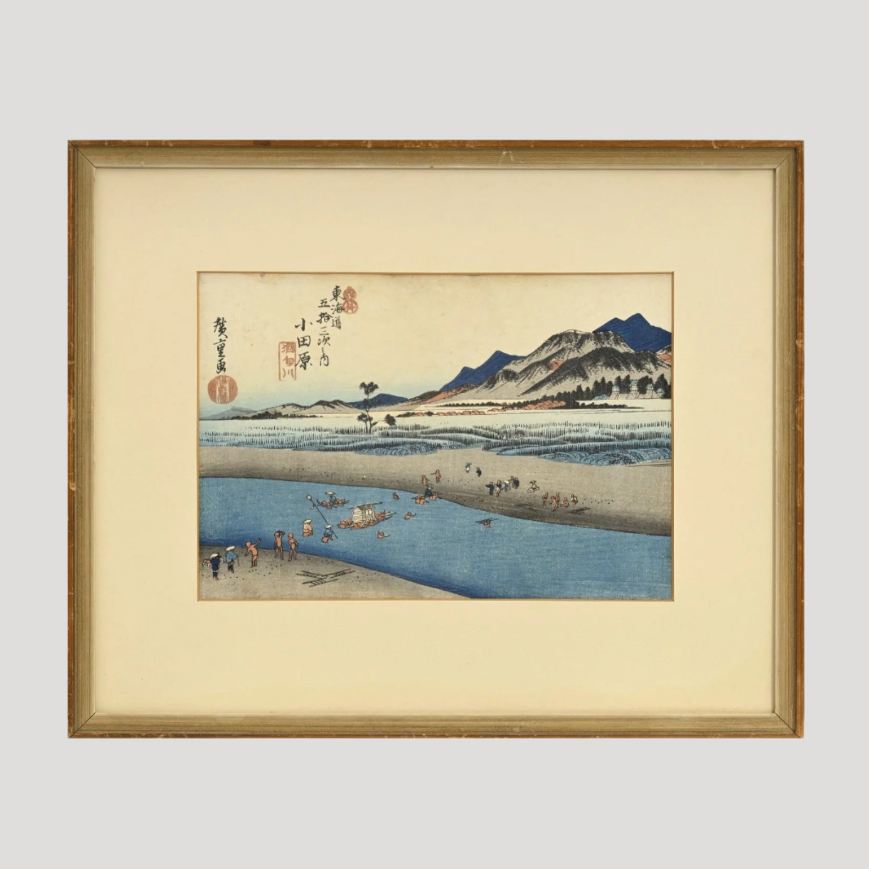 A framed yoko-e print by Utagawa Hiroshige depicting a landscape scene with people and horses on a road, mountains in the background.