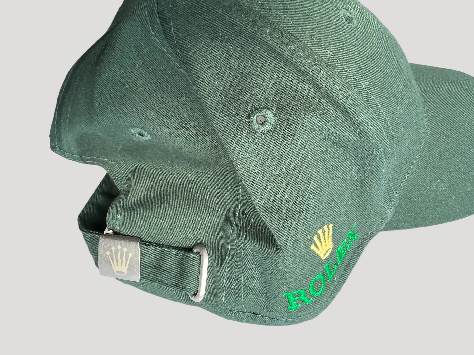 A close-up of a green baseball cap showing the side and back strap, featuring a gold Rolex crown logo and green 'ROLEX' text embroidered on the side.