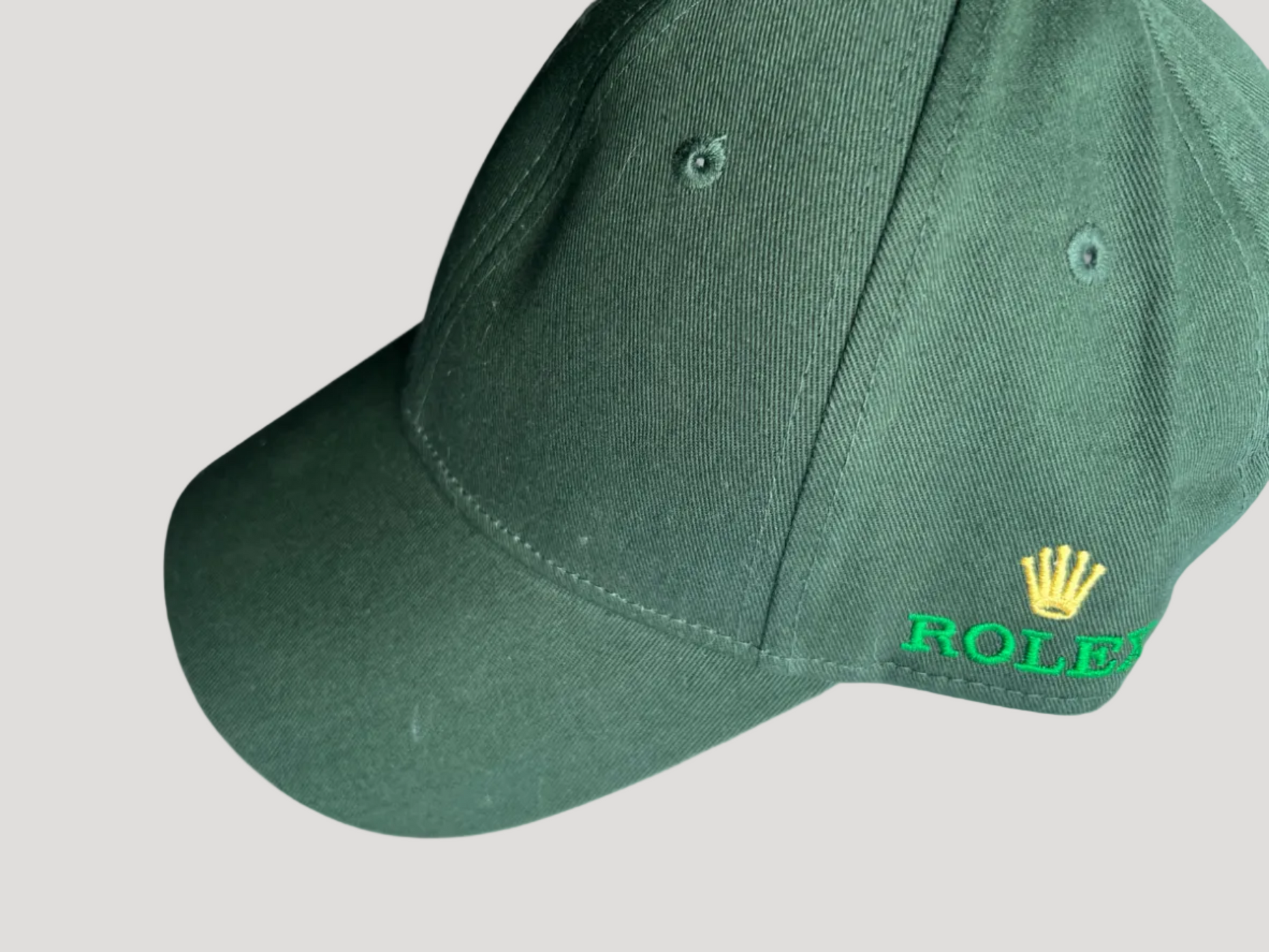 A dark green baseball cap featuring a yellow Rolex crown logo and green 'ROLEX' lettering embroidered on the side, shown against a plain white background.