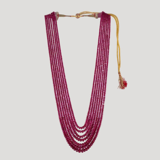 A multi-row necklace of red ruby beads displayed on a white surface, with an adjustable yellow strap.